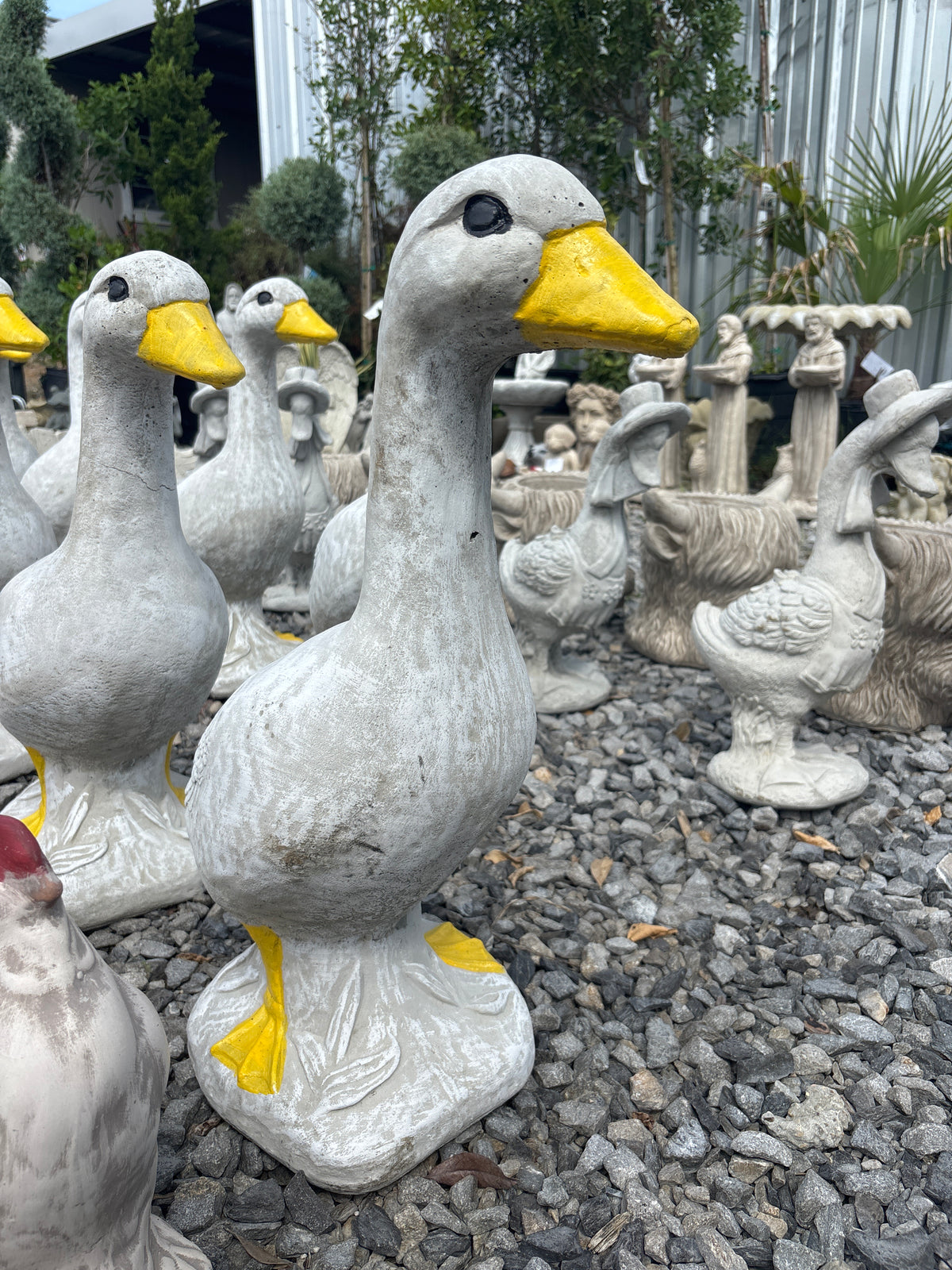 Group of white concrete porch goose statues on gravel